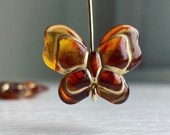 May include: A gold butterfly pendant with amber wings. The wings have a brown and gold color scheme with a glossy finish.