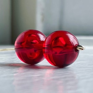 May include: Two large, round, red glass beads strung on a thin gold wire.