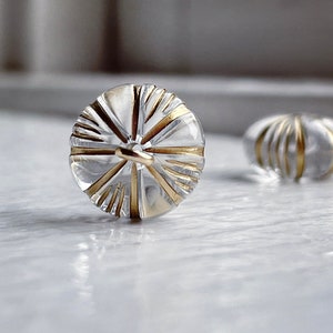 May include: Two clear glass buttons with gold accents. The buttons have a starburst design.