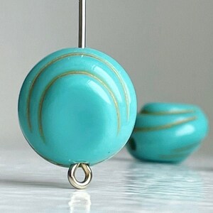 May include: Turquoise blue glass bead with gold stripes and a silver loop. The bead is round and has a glossy finish.