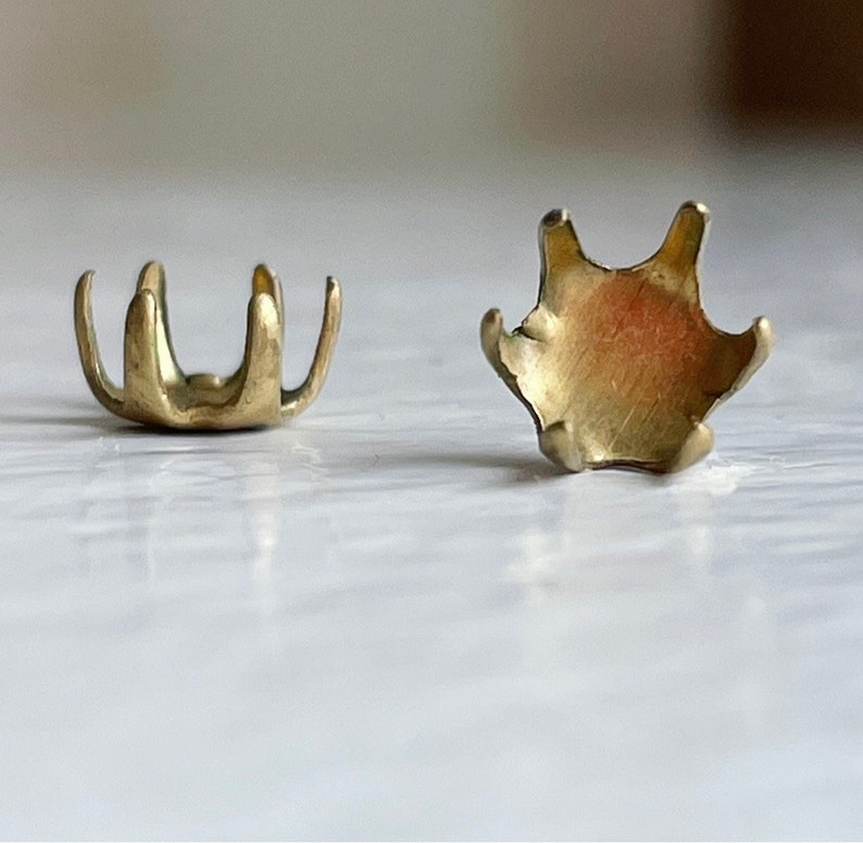May include: Two gold-colored metal settings for a prong setting for a gemstone. The settings are designed to hold a round stone.