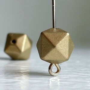 May include: Gold-toned geometric bead with a faceted surface and a silver loop attached. The bead is hanging from a silver wire.