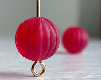 May include: A pair of red glass bead earrings with a gold wire and hook. The beads have a ribbed texture.