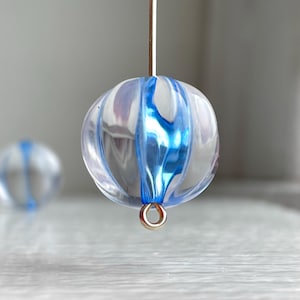 以下が含まれることがあります： 青と白のストライプが入った透明なガラスビーズと、金色の金属製のループ。ビーズは細いワイヤーにぶら下がっています。