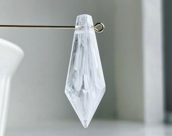 May include: A clear, faceted crystal pendant with a white, marbled design. The pendant is suspended from a gold wire.