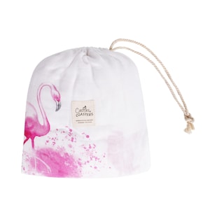 May include: A white muslin swaddle with a pink flamingo and pink watercolor splatter design. The swaddle is in a drawstring bag with a label that reads "Castles & Coasters".