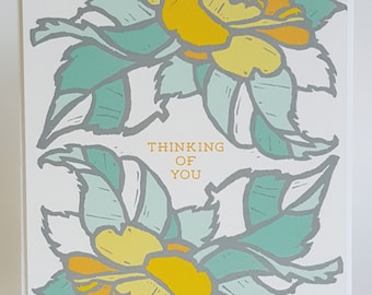 May include: A white card with a floral design in shades of yellow, green, and gray. The text "Thinking of You" is printed in orange on the card.
