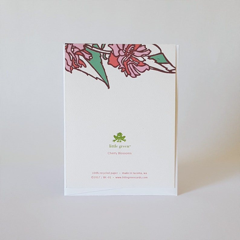 May include: A white card with a green frog logo and the text "little green" and "Cherry Blossoms". The back of the card has a pink and green floral design and the text "100% recycled paper - made in Tacoma, WA &copy;2017/BK-01 www.littlegreencards.com".