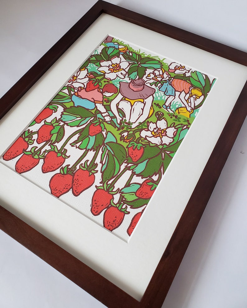 May include: A framed illustration of a strawberry patch with people picking strawberries. The illustration is done in a colorful cartoon style with red strawberries, green leaves, and white flowers.