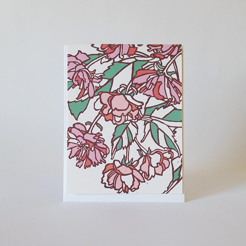 May include: A greeting card with a floral design featuring pink and red flowers with green leaves on a white background.