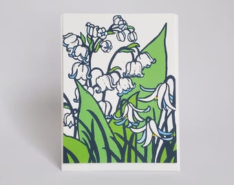 Puede incluir: Una tarjeta blanca con una ilustración verde y azul de flores de lirio de los valles. Las flores son blancas con puntas azules y están rodeadas de hojas verdes.