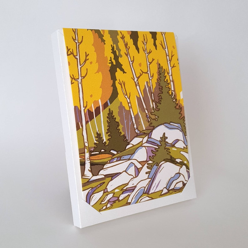 May include: A canvas art print featuring a stylized landscape with yellow and green trees, white birch trees, and blue and gray rocks. The artwork is set against a white background.
