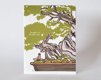 May include: A green and brown illustration of a bonsai tree with a person sitting in front of it. The text "breathe in breathe out" is written on the card.