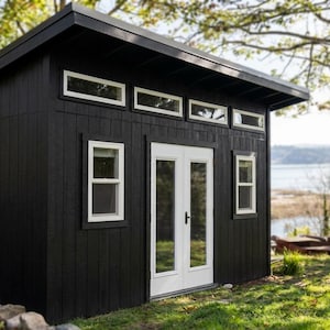 May include: A black shed with vertical siding, a slanted roof, and white-trimmed windows. The structure features a set of double doors with glass panels, four rectangular transom windows above the doors, and two side windows with white frames.