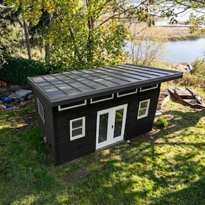 May include: A detached black shed with a flat metal roof, white-framed windows, and a set of white double doors. The structure features horizontal siding and a series of small rectangular windows positioned just below the roofline on the front.
