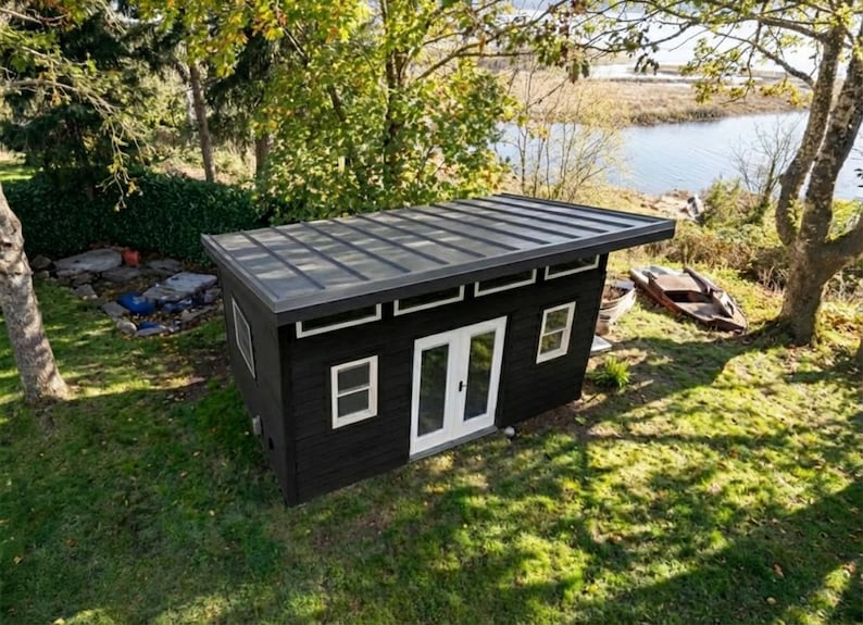 May include: A detached black shed with a flat metal roof, white-framed windows, and a set of white double doors. The structure features horizontal siding and a series of small rectangular windows positioned just below the roofline on the front.