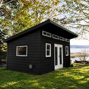 May include: A small, detached shed with black horizontal siding and a single-slope roof. The structure features white-framed windows, a set of white double doors, and a row of four small rectangular transom windows located near the roofline.