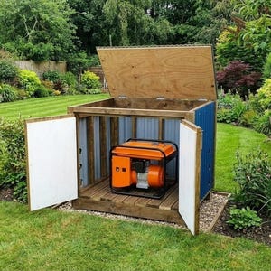 Puede incluir: Un generador naranja dentro de un cobertizo de madera con exterior azul y madera. El cobertizo tiene dos puertas blancas y un techo de madera con bisagras, colocado sobre un lecho de grava. El generador está sobre una plataforma de madera, rodeado de césped y jardín verdes.