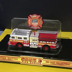 May include: A die-cast Code 3 Fire Engine collectible in a display case. The model is red, white, and yellow with the number 73 on the side. The display case includes a badge with the words "Code 3" and "Fire Department City of New York."