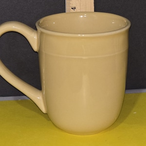 May include: A beige ceramic coffee mug with a rounded handle.