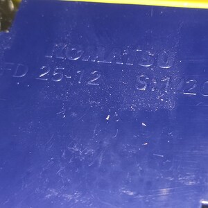 May include: Close-up of a blue plastic part with the text "KOMATSU 25-12 5-1/20" embossed on it.