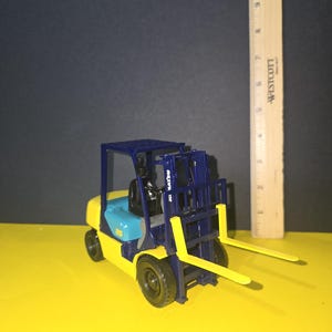 May include: A blue and yellow toy forklift with a black cage and yellow forks. The forklift has the text "TOYOTA" on the side.