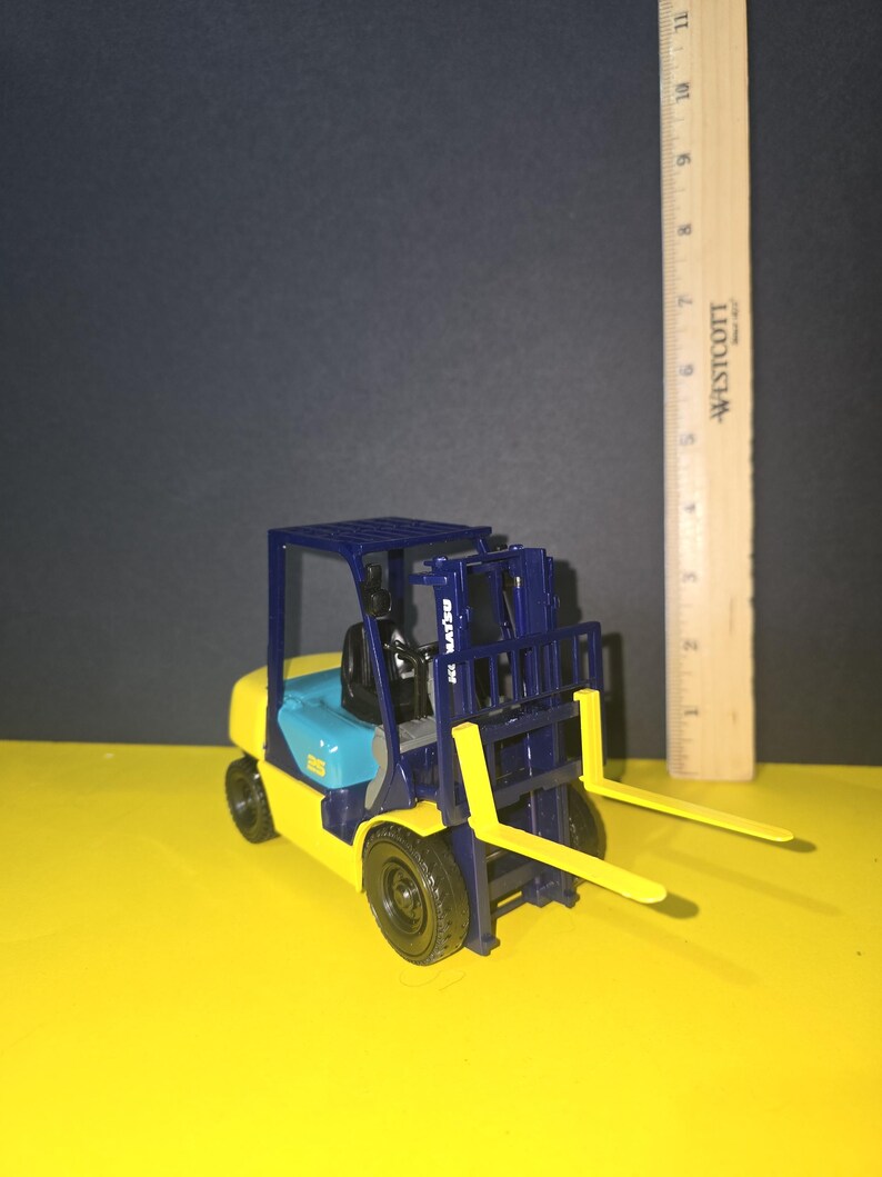 May include: A blue and yellow toy forklift with a black cage and yellow forks. The forklift has the text "TOYOTA" on the side.