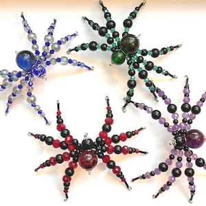May include: Four beaded spider ornaments in blue, green, red, and purple. Each spider has a large, round body and eight legs made of smaller beads. The spiders are handmade and suitable for Halloween or other decorative purposes.