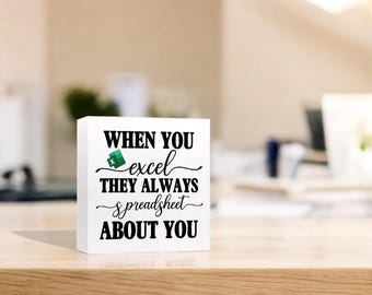 May include: White wooden block with a black and green graphic of the Microsoft Excel logo and the text "When you excel they always spreadsheet about you."