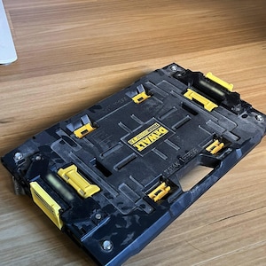 May include: Black and yellow DeWalt TSTAK 2.0 tool storage system. The storage unit has multiple yellow latches and a handle. The text "DeWalt TSTAK 2.0" is visible on the top of the unit. The unit is on wheels.
