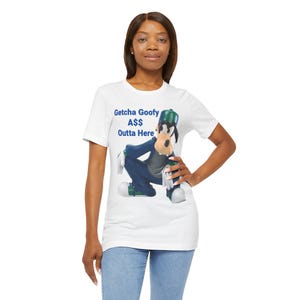 May include: White t-shirt featuring a graphic of Goofy in a blue suit and green hat. The text "Getcha Goofy A$$ Outta Here" is printed above the character. The shirt is worn by a person.