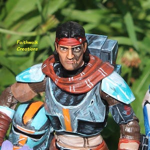 May include: A detailed action figure of a character with a red headband, scar, and a half-painted face. The figure has a gray and blue armored chest and shoulder pads. The text "Faithwalk Creations" is visible.