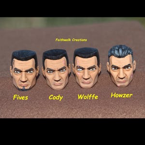 May include: Four hand-painted action figure heads with stern expressions. Each head is a different character, labeled "Fives", "Cody", "Wolffe", and "Howzer". The heads are painted with realistic skin tones and detailed facial features.