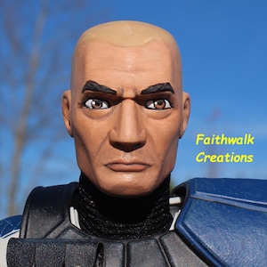 May include: A close-up of a figurine's head, featuring a bald head, dark eyebrows, and brown eyes. The figurine is wearing a black and blue uniform. The text "Faithwalk Creations" is visible in yellow.