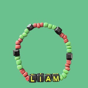 May include: A beaded bracelet with the name "LIAM" spelled out in black and yellow letter beads. The bracelet features green, red, and black beads, set against a solid green background.