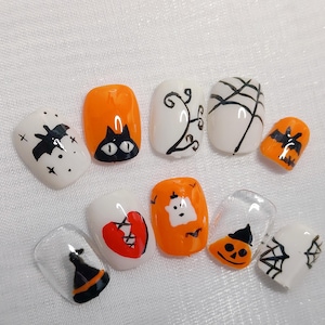 Puede incluir: Diez uñas postizas de color naranja y blanco con temática de Halloween con varios diseños, que incluyen un gato negro, un fantasma, una telaraña, un sombrero de bruja y un corazón roto.
