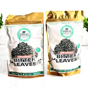 May include: Two bags of grounded bitter leaves. The bags have a gold top and a white front with the text "FIHAJ" and "Grounded Bitter Leaves". The bags are filled with dark green leaves.