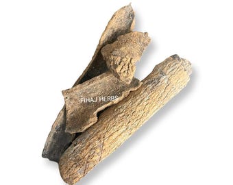 May include: Close-up of dried bark pieces, some are curled and others are straight. The bark is a light brown color and has a rough texture. The text "FIHAJ HERBS" is visible on one of the pieces.