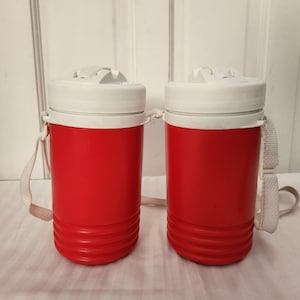 May include: Two red insulated beverage containers with white lids and carrying straps. The containers have a ribbed design.