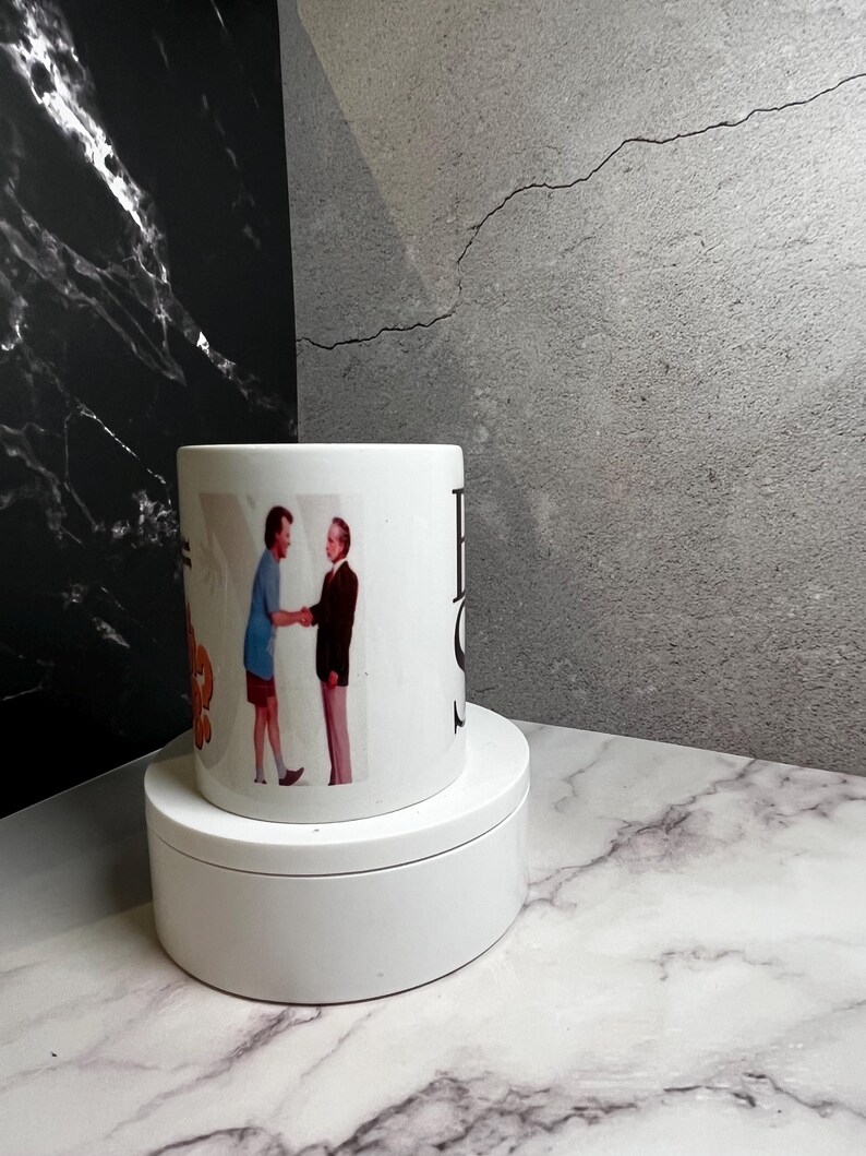 May include: White ceramic mug with a vintage image of two people shaking hands. The mug has the words "Best Of" printed on it. The mug is displayed on a white, round platform.