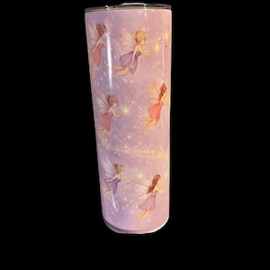Peut inclure: Un gobelet cylindrique et haut avec un fond violet clair. Le gobelet est décoré d'illustrations de fées dans diverses poses, tenant des baguettes lumineuses. Les fées sont représentées avec des robes et des ailes colorées.