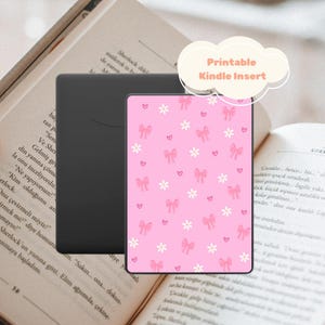 Può includere: Un inserto rosa per Kindle con un motivo di fiori bianchi, fiocchi rosa e piccoli cuori. L'inserto è accanto a un dispositivo Kindle nero e a un libro aperto. Il testo "Printable Kindle Insert" è in una nuvola.