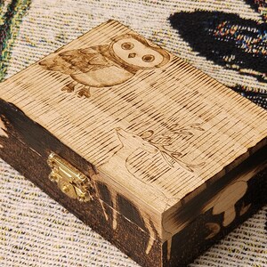 Peut inclure: Une boîte en bois avec un couvercle à charnières, ornée d'un motif de hibou et de cerf brûlé au bois. La boîte est munie d'un loquet en laiton et d'une teinture brun foncé autour des bords.