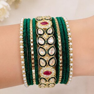 May include: A collection of green velvet bangles, accented with gold-toned metal and embellished with clear and red gemstones. The set includes pearl-like beaded bracelets.