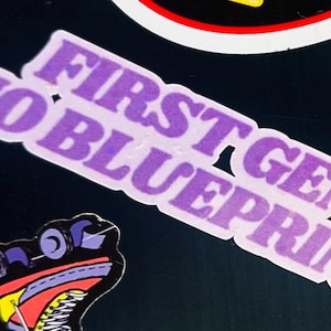 May include: A purple sticker with the text "FIRST GEN NO BLUEPRINT" in white outline. The sticker is angled across the image. Other stickers are partially visible in the background.