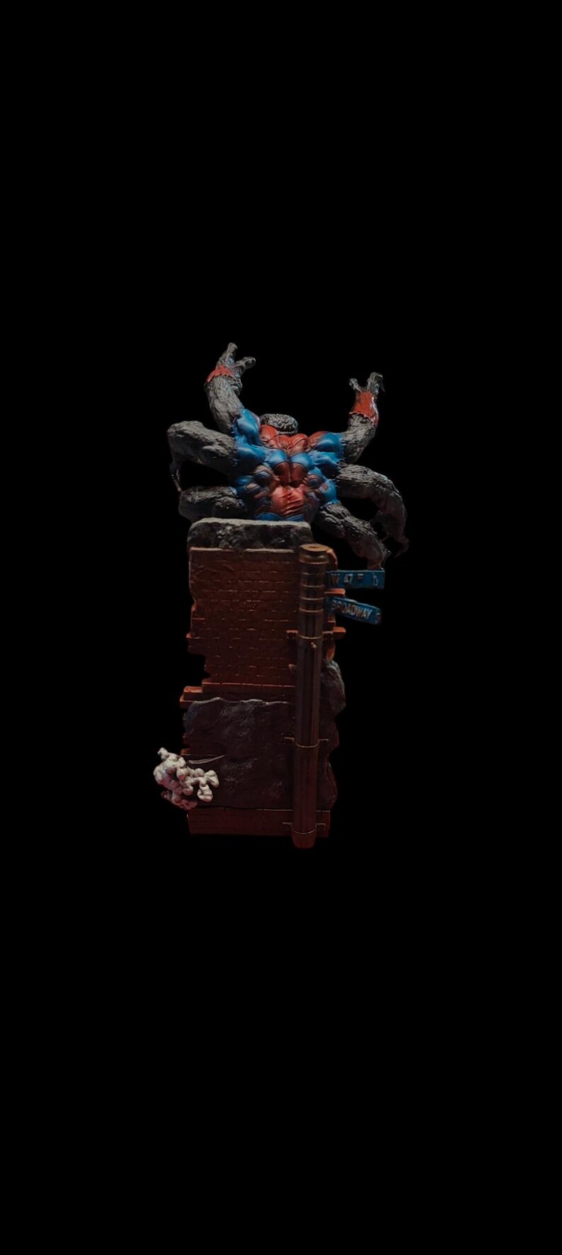May include: A black and red action figure of a spider-like creature with multiple arms, standing on a broken brick wall with a blue street sign that reads "47th St Broadway".