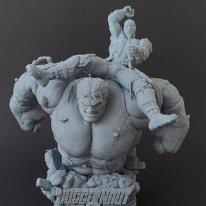 Puede incluir: Una figura gris impresa en 3D del personaje de Marvel Comics Juggernaut, con el texto "JUGGERNAUT" en la base. La figura representa a Juggernaut con una figura m&aacute;s peque&ntilde;a de Wolverine montada en su espalda.