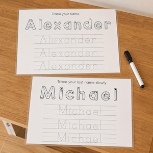 May include: Two white rectangular laminated practice sheets for handwriting. The top sheet features the name Alexander with tracing lines, and the bottom sheet features the name Michael with tracing lines. A black dry-erase marker is included.