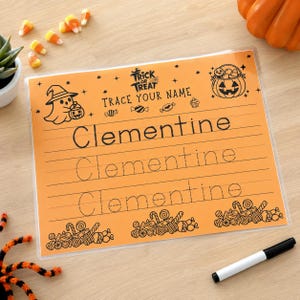 May include: A rectangular orange Halloween-themed dry-erase tracing sheet with the text Trick or Treat Trace Your Name and the name Clementine printed in dotted lines. The sheet features black illustrations of a ghost, a jack-o'-lantern, and candy.