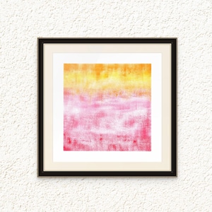 May include: Abstract art print in a black frame. The artwork features a gradient of colors, transitioning from yellow to pink. The textured surface adds depth to the piece, creating a visually appealing composition. The framed art is mounted on a white textured wall.
